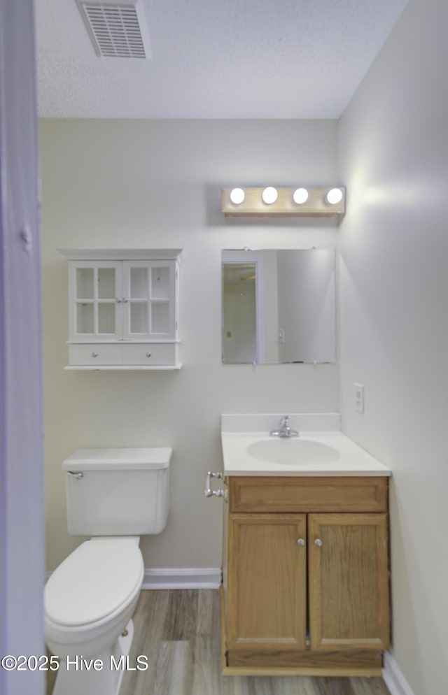 half bath with toilet, wood finished floors, vanity, visible vents, and baseboards