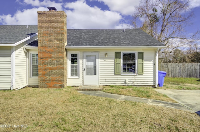 view of front of house featuring a shingled roof, fence, a chimney, and a front lawn