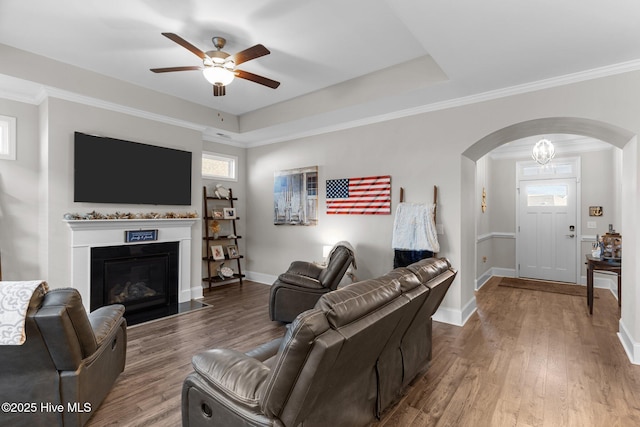 living area with baseboards, ceiling fan, wood finished floors, arched walkways, and a raised ceiling