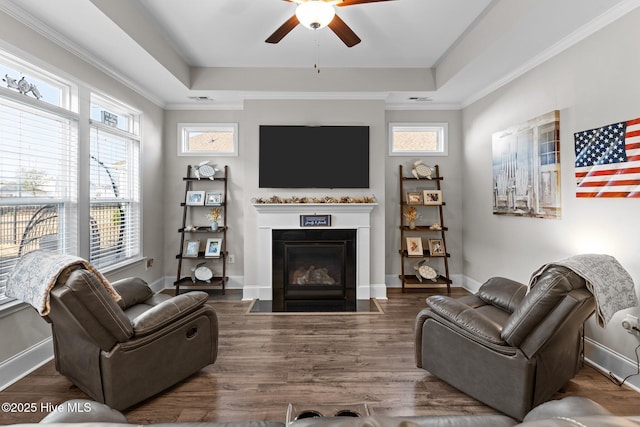 living room with a wealth of natural light, a fireplace with flush hearth, a raised ceiling, and a ceiling fan