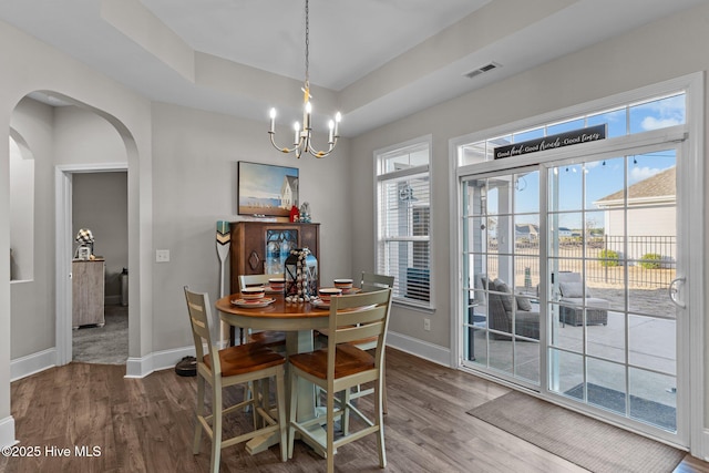 dining room featuring visible vents, a tray ceiling, wood finished floors, arched walkways, and a chandelier