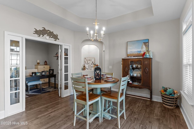 dining space with arched walkways, a chandelier, a tray ceiling, and wood finished floors