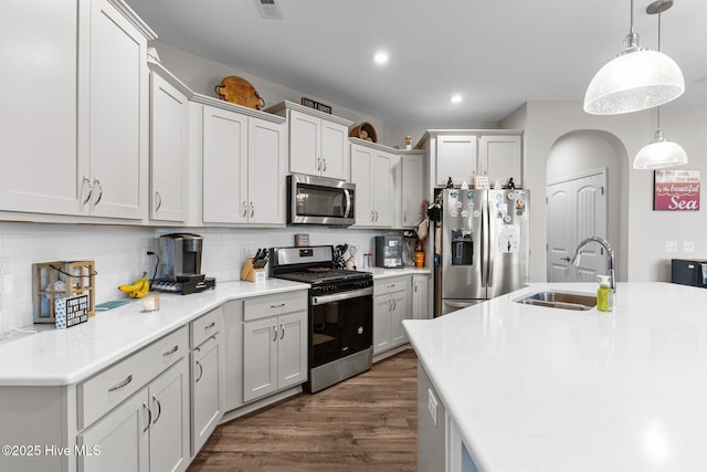 kitchen with tasteful backsplash, dark wood-type flooring, decorative light fixtures, stainless steel appliances, and a sink