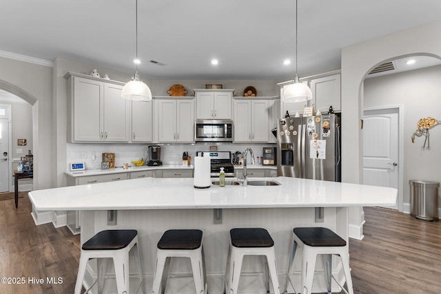 kitchen featuring backsplash, dark wood-style floors, appliances with stainless steel finishes, arched walkways, and a sink