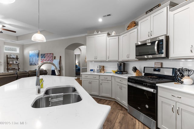 kitchen with a sink, stainless steel appliances, arched walkways, decorative backsplash, and dark wood-style flooring