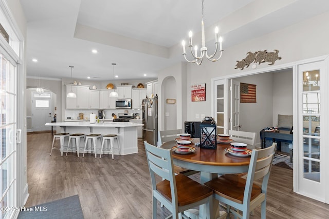 dining area featuring light wood finished floors, an inviting chandelier, a tray ceiling, recessed lighting, and arched walkways