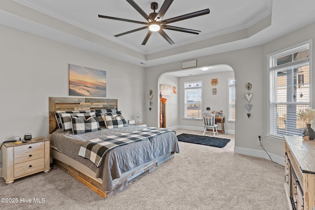 bedroom featuring arched walkways, light colored carpet, a raised ceiling, and baseboards