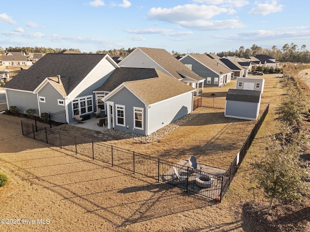 rear view of property featuring a residential view, roof with shingles, an outdoor structure, a fenced backyard, and a patio area