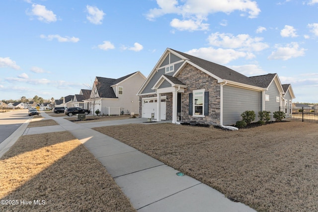 view of front of property featuring stone siding, a residential view, driveway, and fence