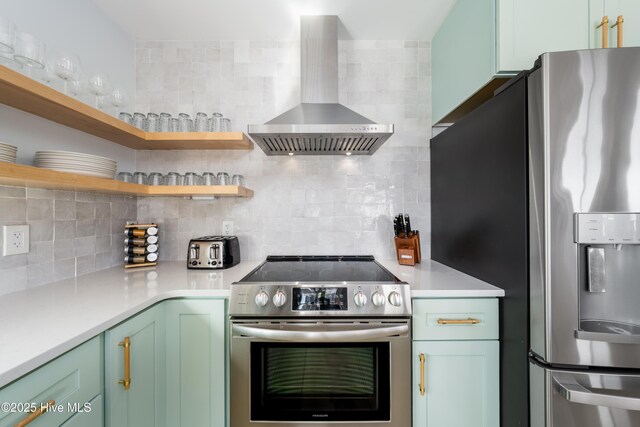 kitchen with tasteful backsplash, stainless steel appliances, light countertops, wall chimney range hood, and green cabinets