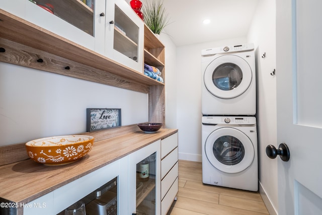 washroom featuring baseboards, laundry area, wood finish floors, and stacked washer / drying machine