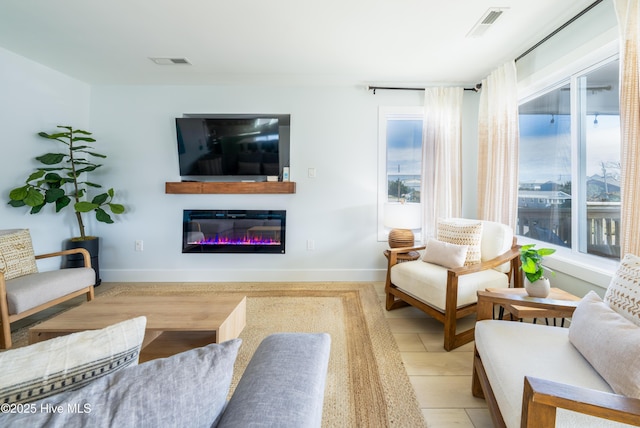 living room featuring a glass covered fireplace, visible vents, and baseboards