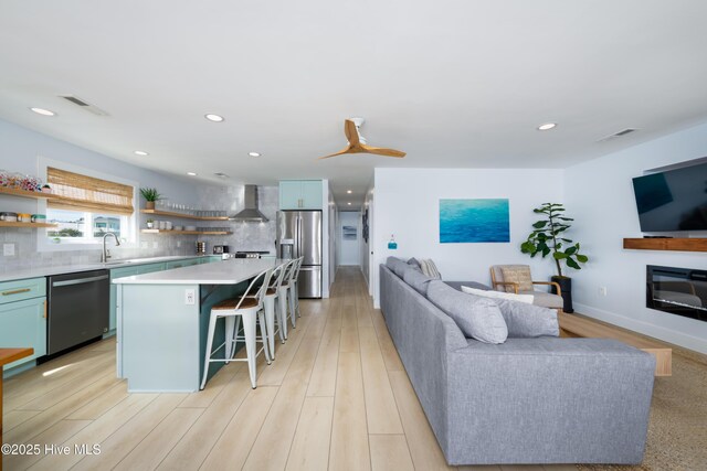 kitchen with visible vents, open floor plan, stainless steel appliances, wall chimney range hood, and open shelves