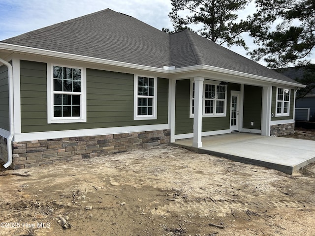 rear view of property with stone siding, a patio, and roof with shingles