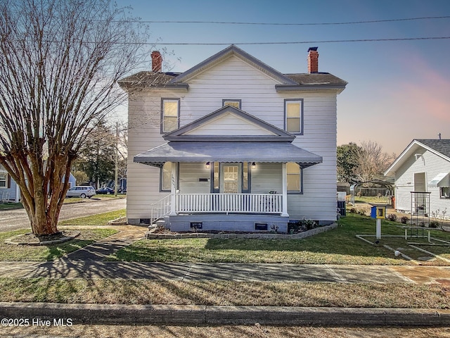 view of front of house with covered porch, a chimney, and a front yard