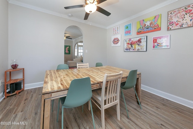 dining space with arched walkways, crown molding, ceiling fan, wood finished floors, and baseboards