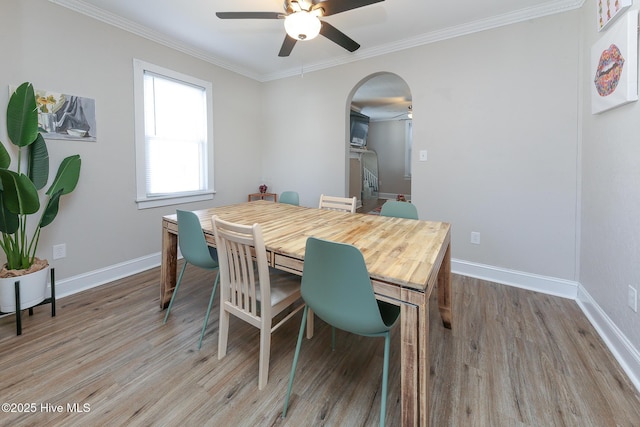 dining space with ornamental molding, arched walkways, baseboards, and light wood finished floors