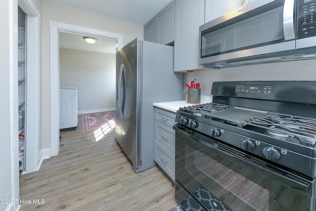 kitchen featuring washer / clothes dryer, light countertops, appliances with stainless steel finishes, gray cabinets, and light wood finished floors