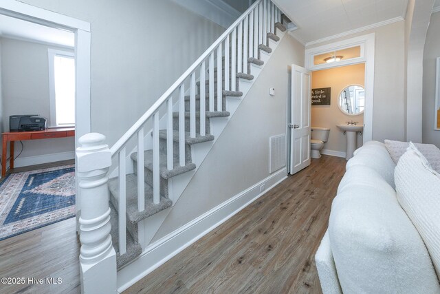 staircase with ornamental molding, wood finished floors, visible vents, and baseboards