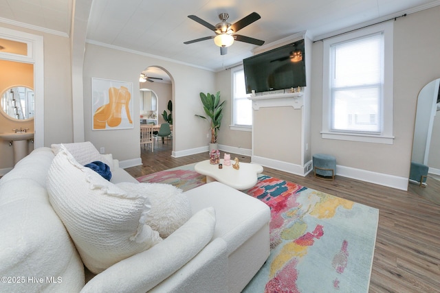 living room featuring ornamental molding, arched walkways, baseboards, and wood finished floors