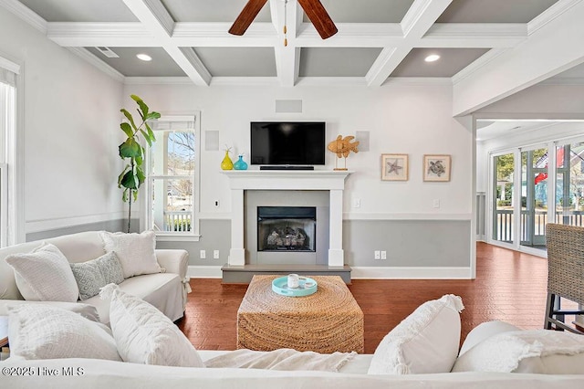 living room featuring baseboards, a fireplace with raised hearth, beam ceiling, and wood finished floors