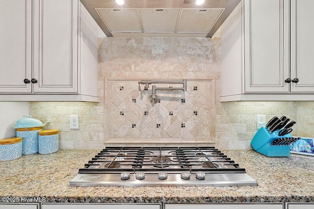 kitchen featuring stainless steel gas cooktop, backsplash, light stone countertops, and range hood