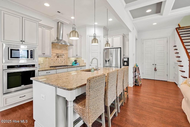 kitchen with light stone counters, stainless steel appliances, dark wood-type flooring, a sink, and wall chimney range hood