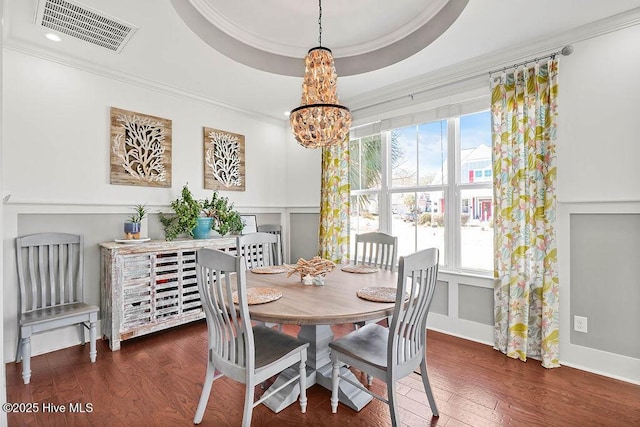 dining area featuring crown molding, a notable chandelier, a raised ceiling, visible vents, and wood finished floors