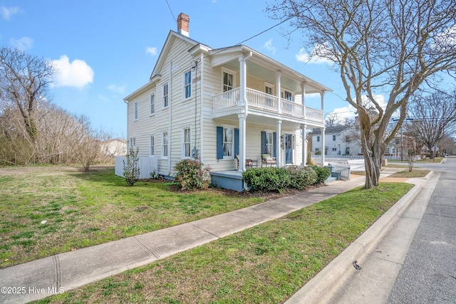 view of front of house with a porch, a balcony, a front yard, and a chimney