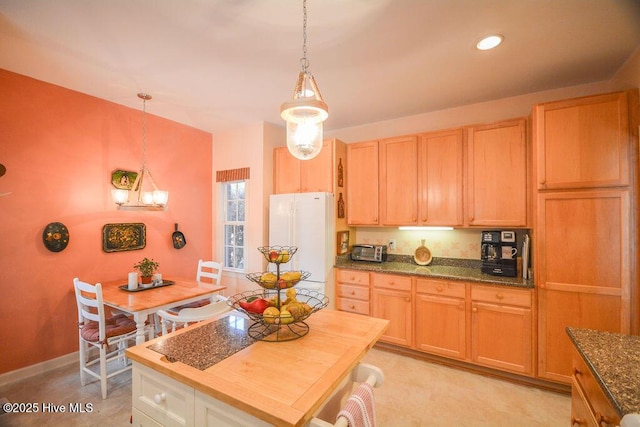 kitchen featuring baseboards, a toaster, dark stone countertops, freestanding refrigerator, and hanging light fixtures