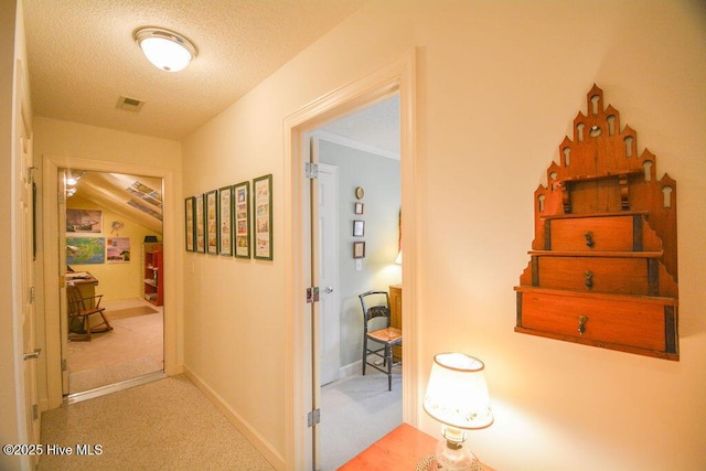 hallway with carpet flooring, visible vents, a textured ceiling, and baseboards