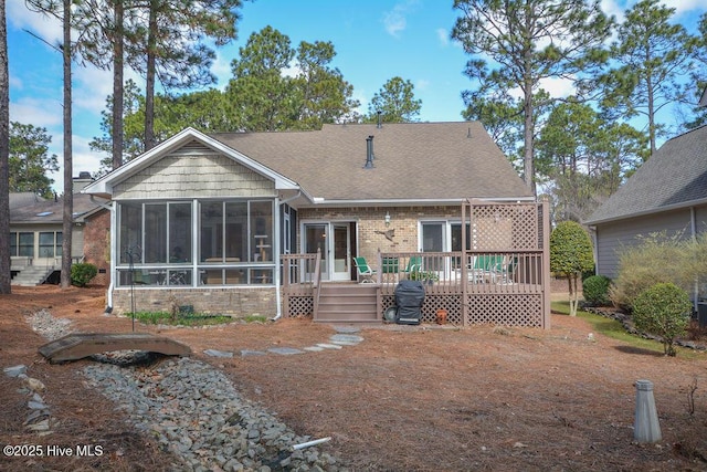 rear view of property featuring brick siding, a shingled roof, a deck, and a sunroom