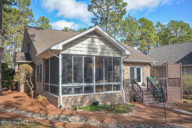 rear view of property with a shingled roof, a wooden deck, and a sunroom