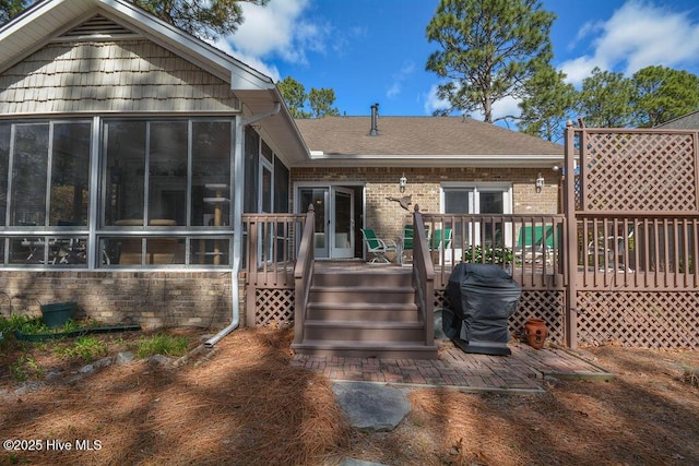 rear view of house featuring brick siding, roof with shingles, a deck, and a sunroom