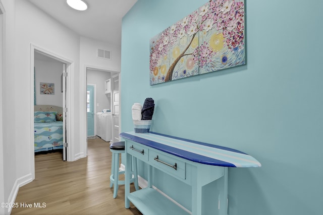 hall with washing machine and clothes dryer, visible vents, light wood-type flooring, and baseboards