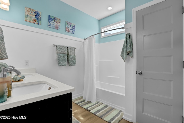 full bath featuring double vanity, wood finished floors, shower / bath combo with shower curtain, and a sink