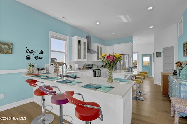 kitchen with wood finished floors, a breakfast bar, light countertops, appliances with stainless steel finishes, and wall chimney range hood