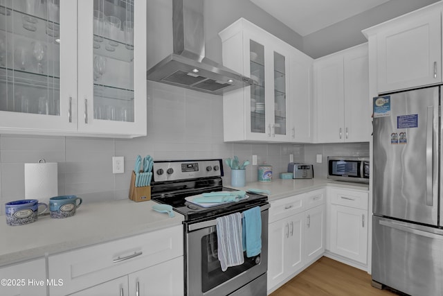 kitchen with tasteful backsplash, glass insert cabinets, wall chimney range hood, stainless steel appliances, and white cabinetry