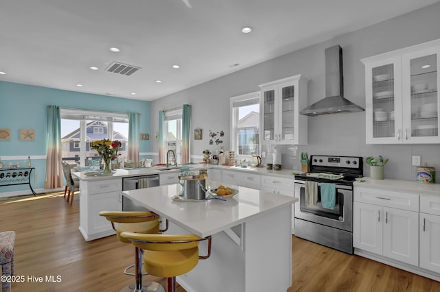 kitchen featuring wall chimney exhaust hood, light wood-style floors, visible vents, and appliances with stainless steel finishes