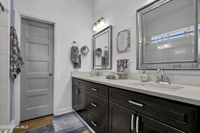 full bath featuring double vanity, a tile shower, wood finished floors, and a sink