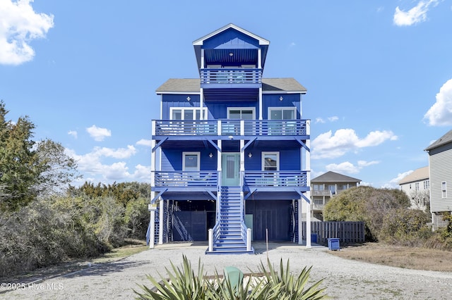 coastal inspired home featuring gravel driveway, covered porch, stairs, a carport, and board and batten siding