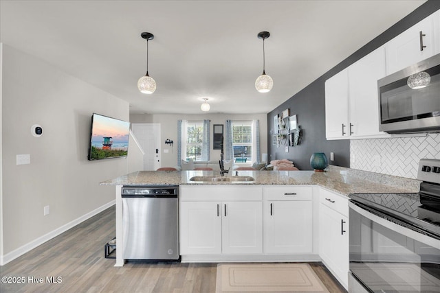 kitchen featuring tasteful backsplash, appliances with stainless steel finishes, a peninsula, pendant lighting, and a sink