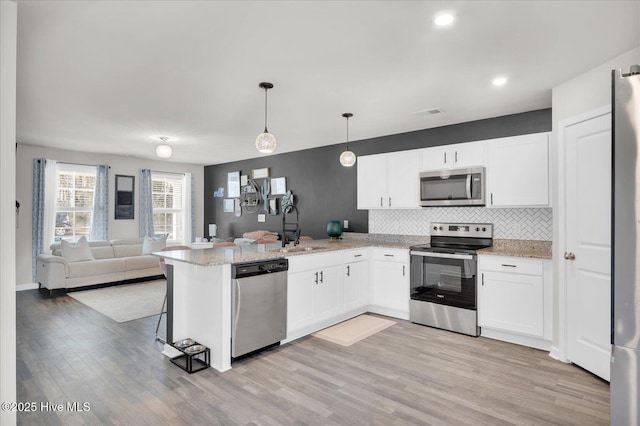 kitchen with a peninsula, a sink, white cabinetry, open floor plan, and appliances with stainless steel finishes