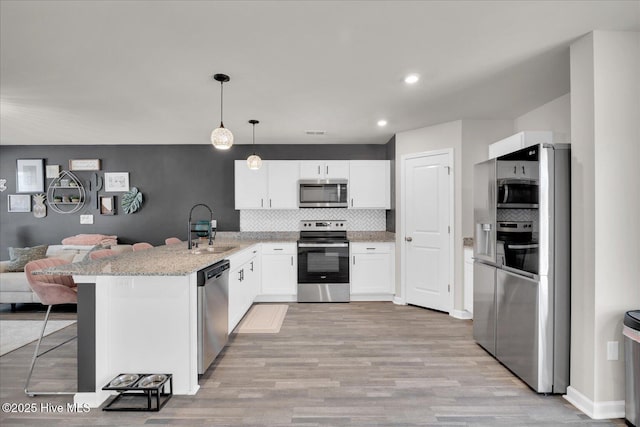 kitchen with stainless steel appliances, a peninsula, a sink, open floor plan, and light stone countertops