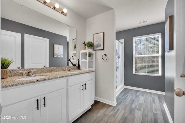 full bathroom with double vanity, visible vents, a sink, and wood finished floors