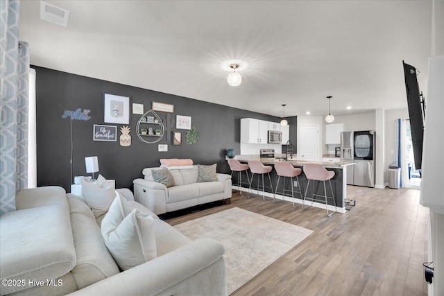 living room featuring light wood-style floors, an accent wall, visible vents, and recessed lighting