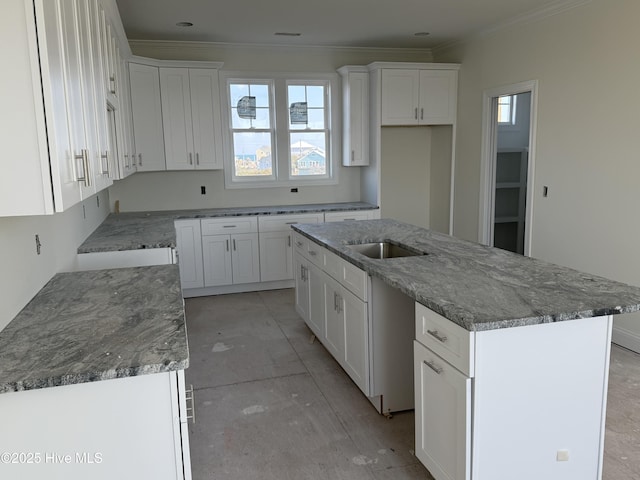 kitchen featuring ornamental molding, a sink, a kitchen island with sink, and white cabinetry