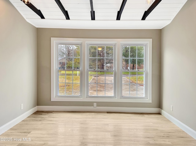 unfurnished room featuring lofted ceiling with beams, light wood-style flooring, and baseboards