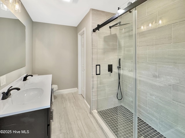 bathroom with double vanity, a shower stall, baseboards, and a sink