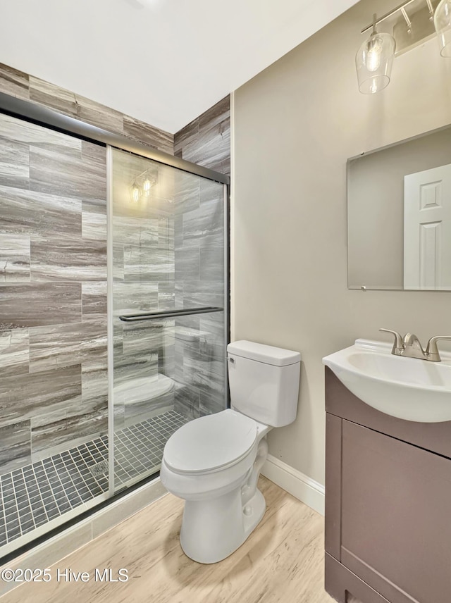 full bath with toilet, wood finished floors, a shower stall, baseboards, and vanity